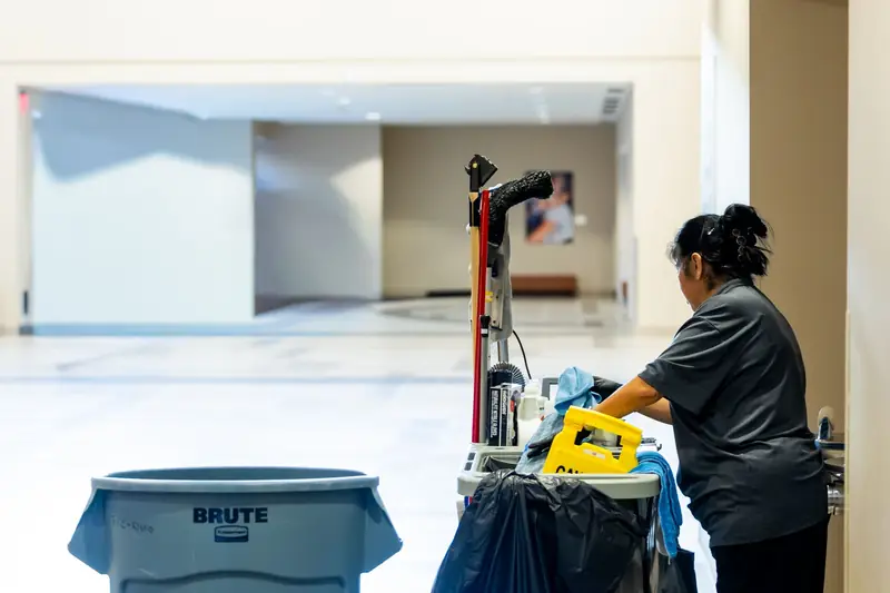Janitorial worker pushing a cleaning cart down a building hallway